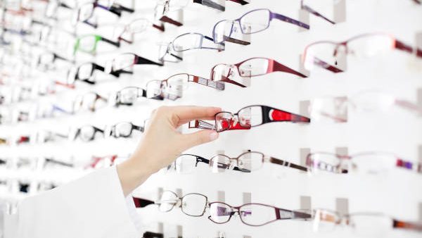 Optician suggest glasses. Closeup showing many eyeglasses in background.